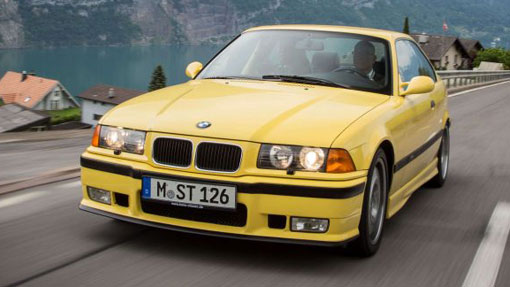 Image of yellow BMW M3 driving on a road next to an alpine lake
