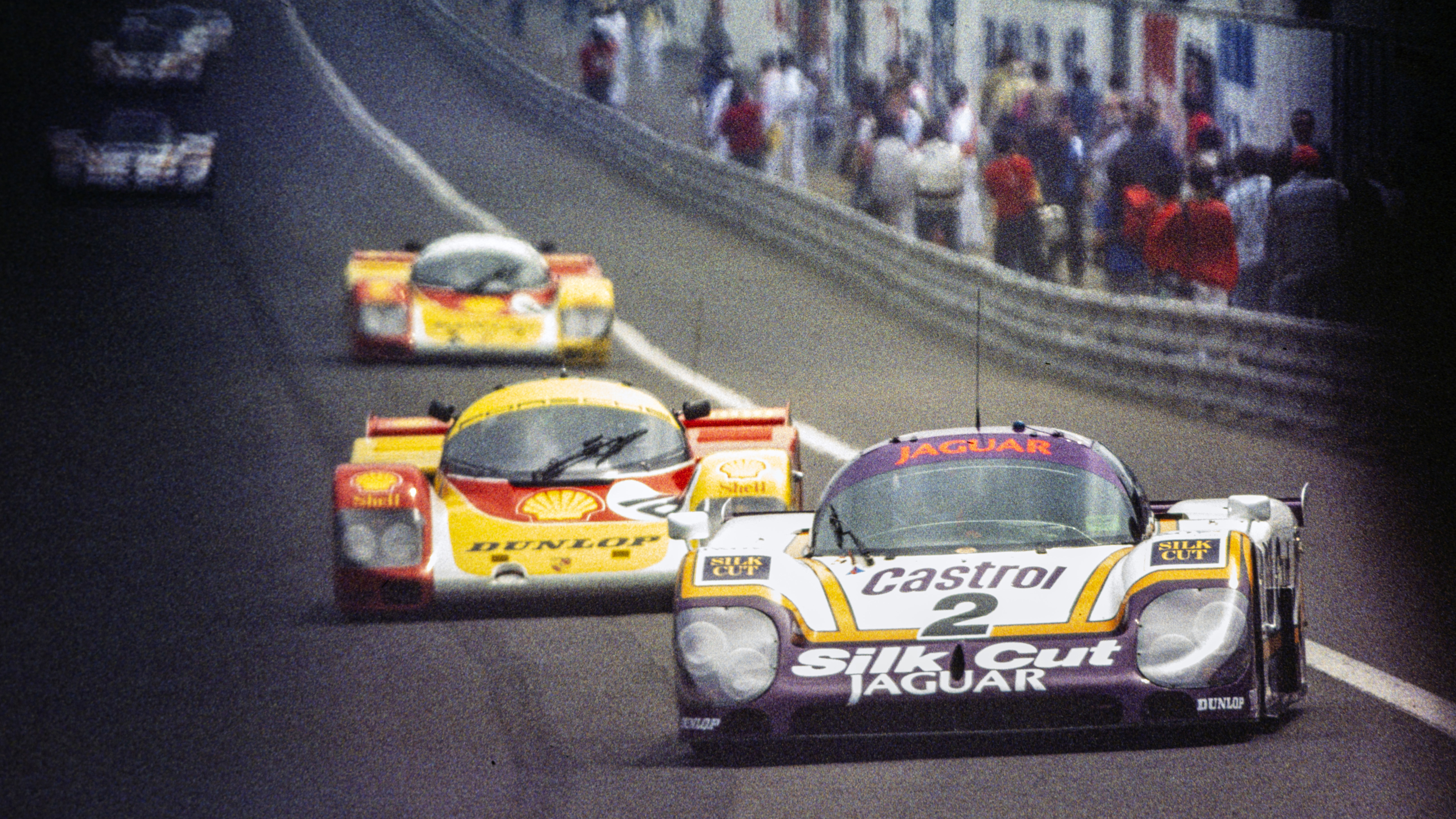 Two cars with striking liveries. The Lammers/Dumfries/Wallace Jaguar XJR-9 LM leads its Porsche 962 C rivals at the 1988 Le Mans 24 Hours. 